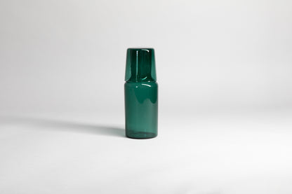 Transparent green carafe with matching glass cup flipped upside down on carafe top of carafe. Set on a light gray background