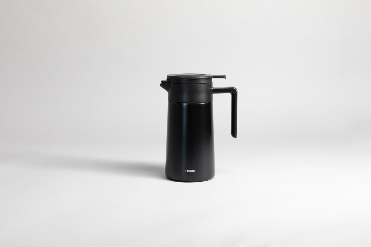 Black cylincial pot with an black polypropylene spout, handle and lid. Set on a light gray background.
