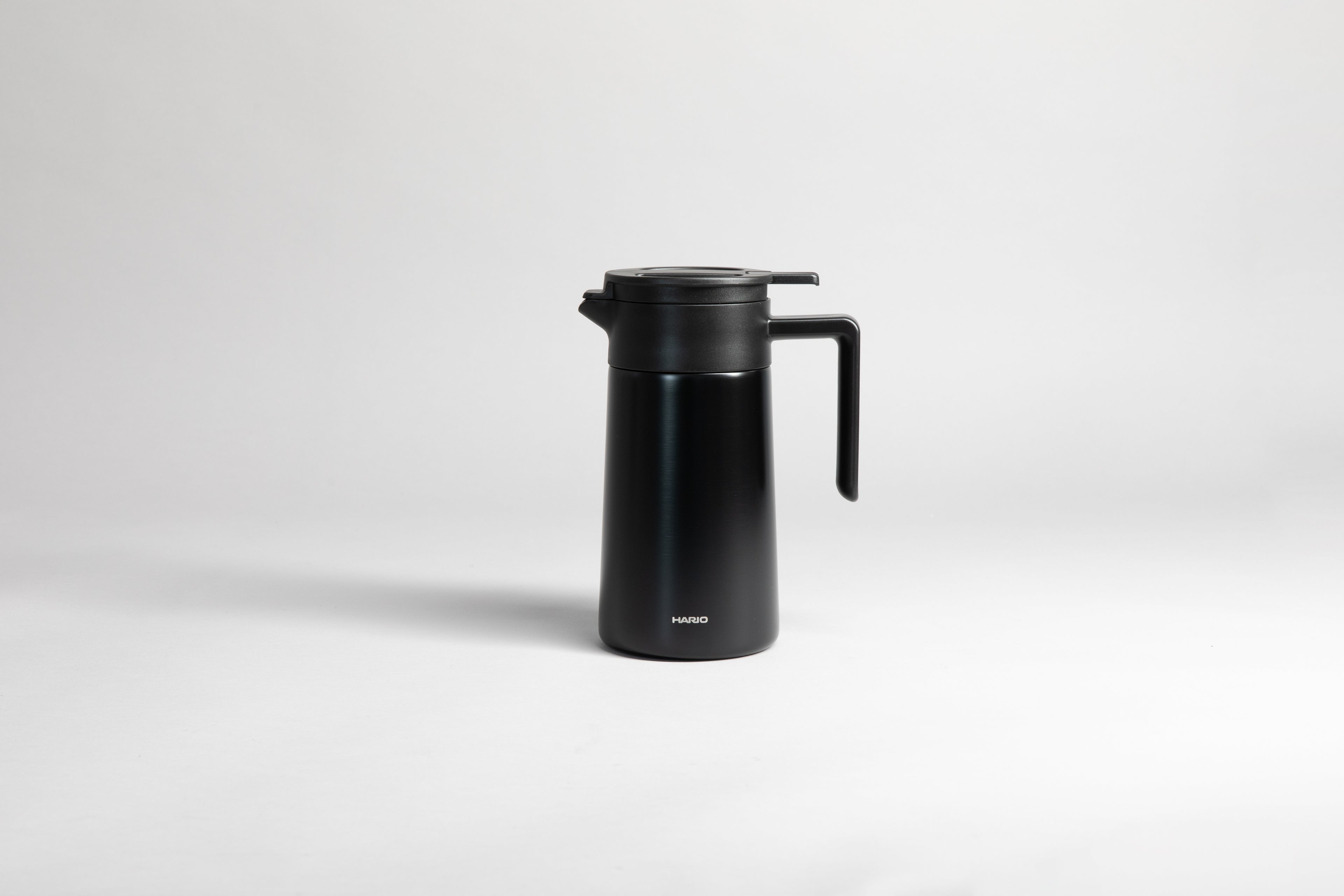 Black cylincial pot with an black polypropylene spout, handle and lid. Set on a light gray background.