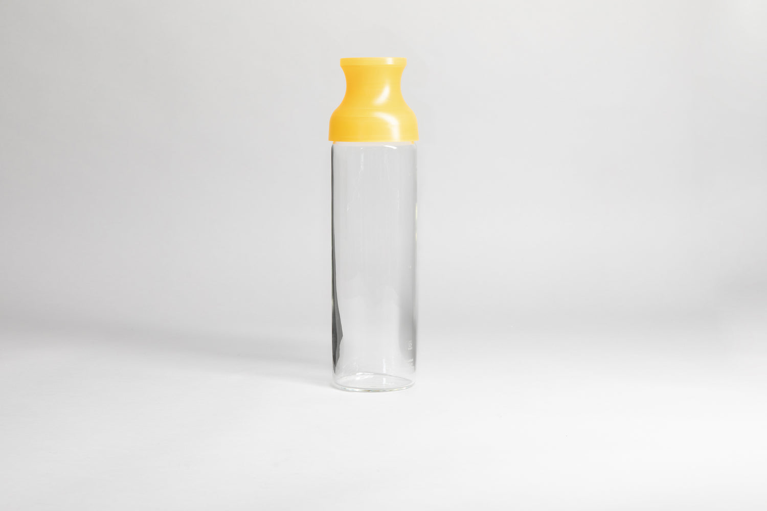Cylindrical glass bottle with a clear yellow silicone wide mouth spout. set on a white background