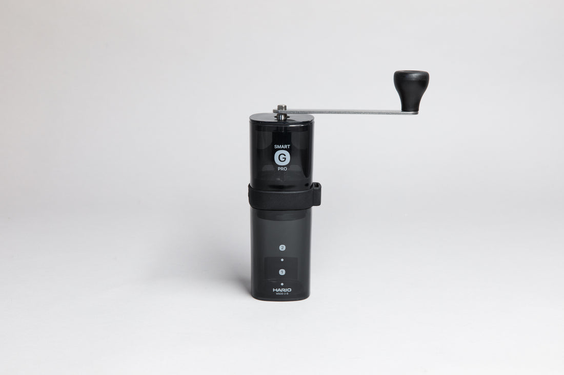 Black transparent plastic coffee mill with a slim metal handle attached to the shaft of the grinder.