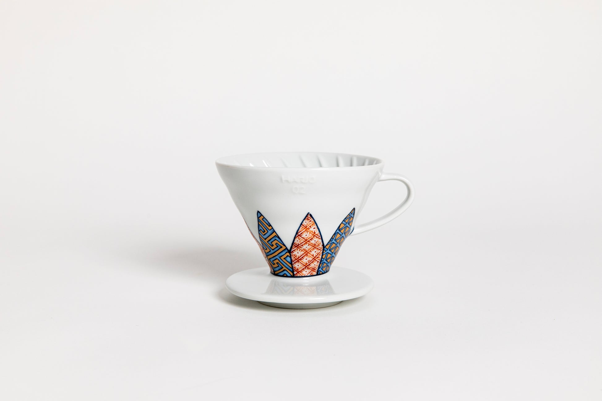 White cone-shaped ceramic coffee dripper with handle and round base, featuring Shonzui (祥瑞) pattern with auspicious symbols like pine, bamboo, and plum blossoms on a geometric tortoise-shell design. set on a white backaground.