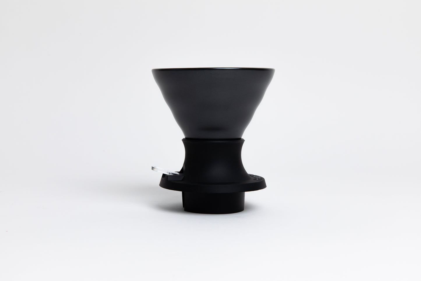 Cone-shaped matte black ceramic dripper seated in a black silicone base with clear plastic push switch on a white background.