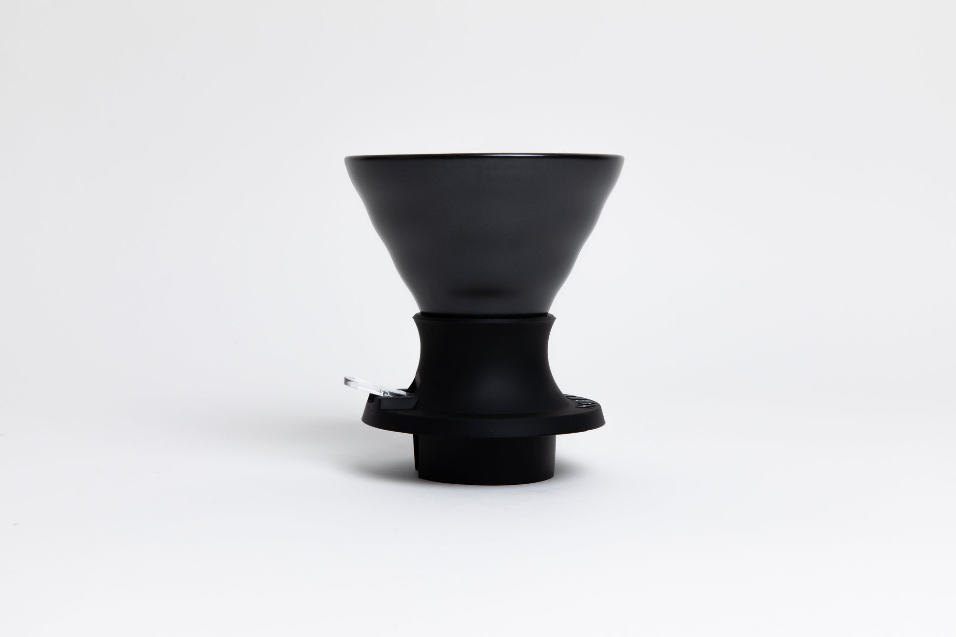 Cone-shaped matte black ceramic dripper seated in a black silicone base with clear plastic push switch on a white background.