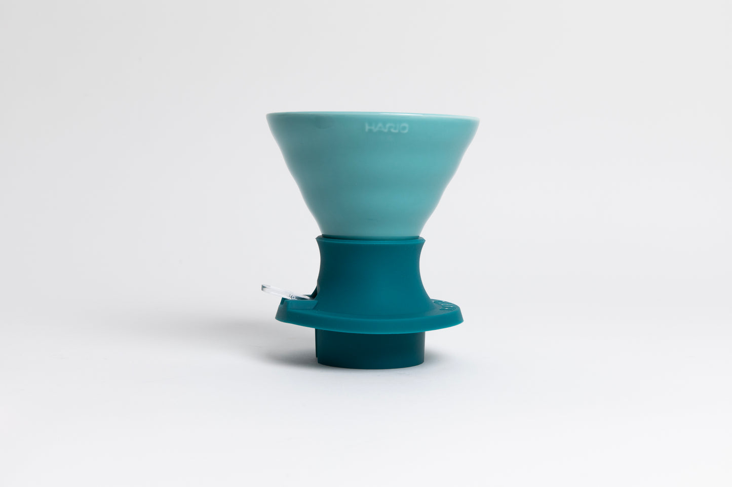 Cone-shaped turquoise ceramic dripper seated in a dark turquoise silicone base with clear plastic push switch on a white background.