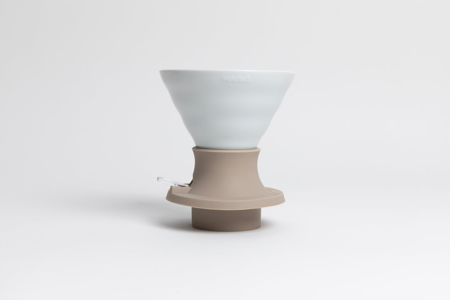 Cone-shaped matte white ceramic dripper seated in a light tan silicone base with clear plastic push switch on a white background.