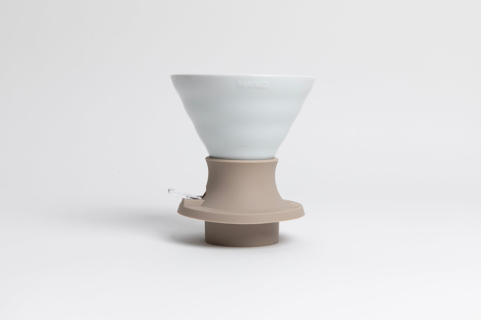 Cone-shaped matte white ceramic dripper seated in a light tan silicone base with clear plastic push switch on a white background.
