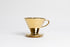 Metallic gold cone shaped ceramic coffee dripper with handle and round base. Set on white background
