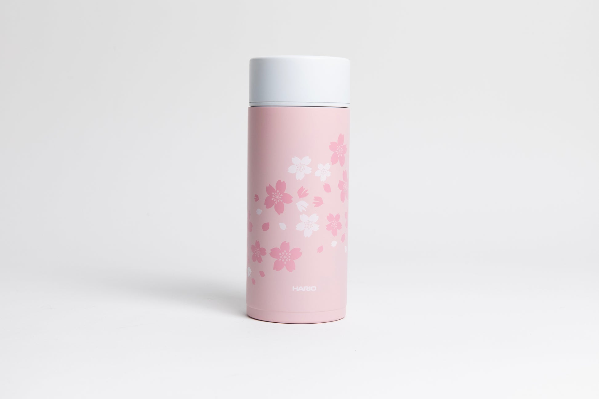Cylindrical pink bottle with dark pink and white sakura blossoms design with a white lid. set on a white bckground.