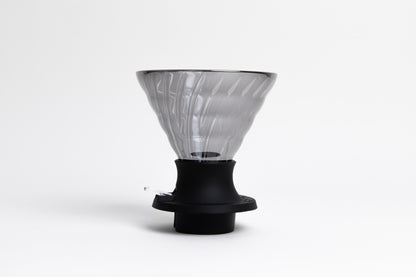 large cone-shaped clear black glass coffee dripper in a black silicone base with clear plastic push switch. set on a white background