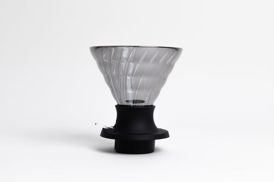 large cone-shaped clear black glass coffee dripper in a black silicone base with clear plastic push switch. set on a white background
