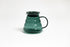 All glass transparent dark green beehive shaped coffee server with glass handle and glass lid with dark plastic rubber gasket on white backdrop.