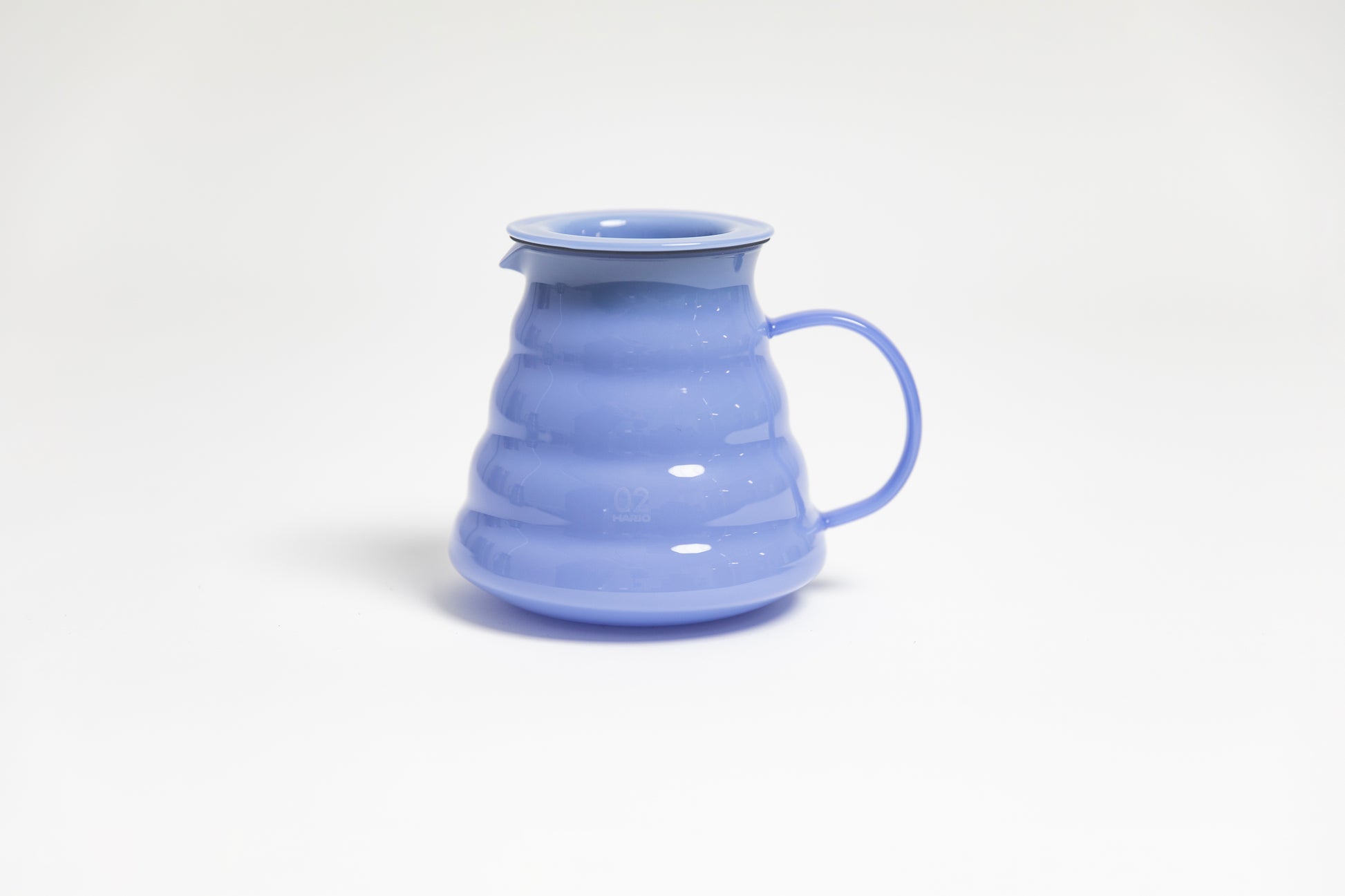 All glass milky purple beehive shaped coffee server with handle and glass lid on white backdrop
