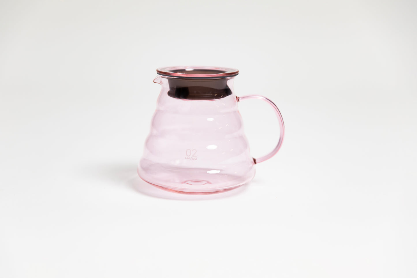 All glass transparent pink beehive shaped coffee server with glass handle and glass lid with dark plastic rubber gasket on white backdrop.