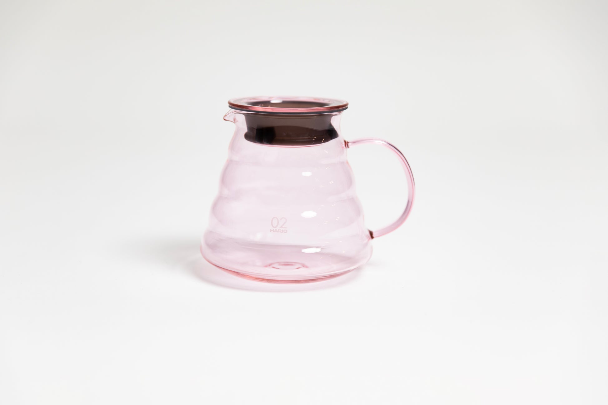 All glass transparent pink beehive shaped coffee server with glass handle and glass lid with dark plastic rubber gasket on white backdrop.
