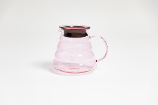 All glass transparent pink beehive shaped coffee server with glass handle and glass lid with dark plastic rubber gasket on white backdrop.