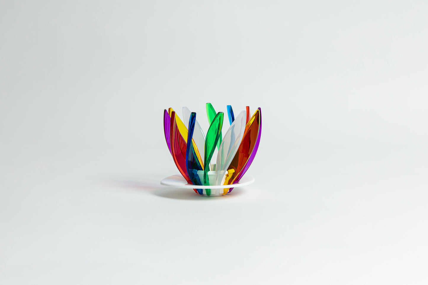 Transparent rainbow in the colors red, blue, green, white, orange, purple and yellow pedals in a spiral shape on a transparent black base on a white background.