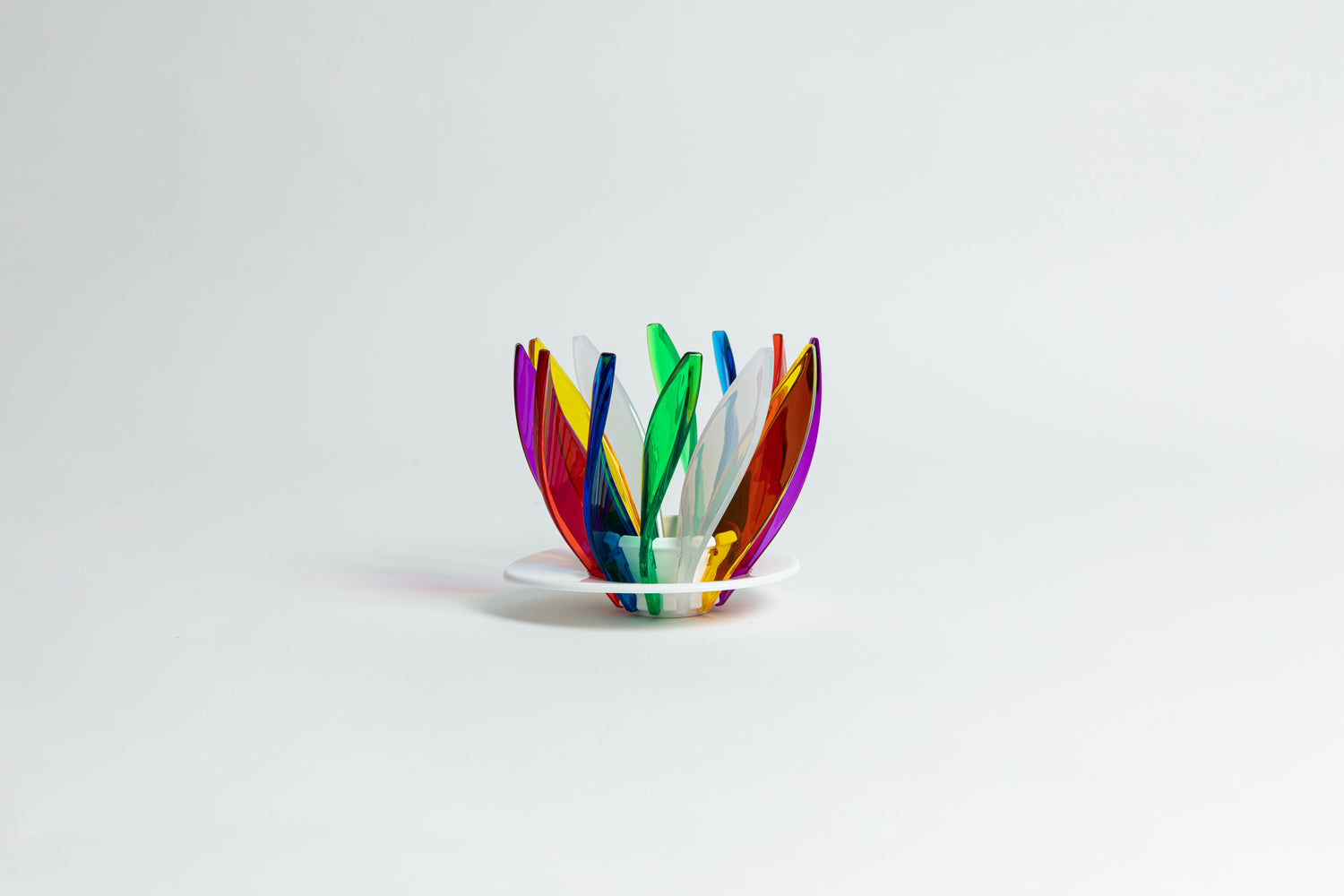 Transparent rainbow in the colors red, blue, green, white, orange, purple and yellow pedals in a spiral shape on a transparent black base on a white background.