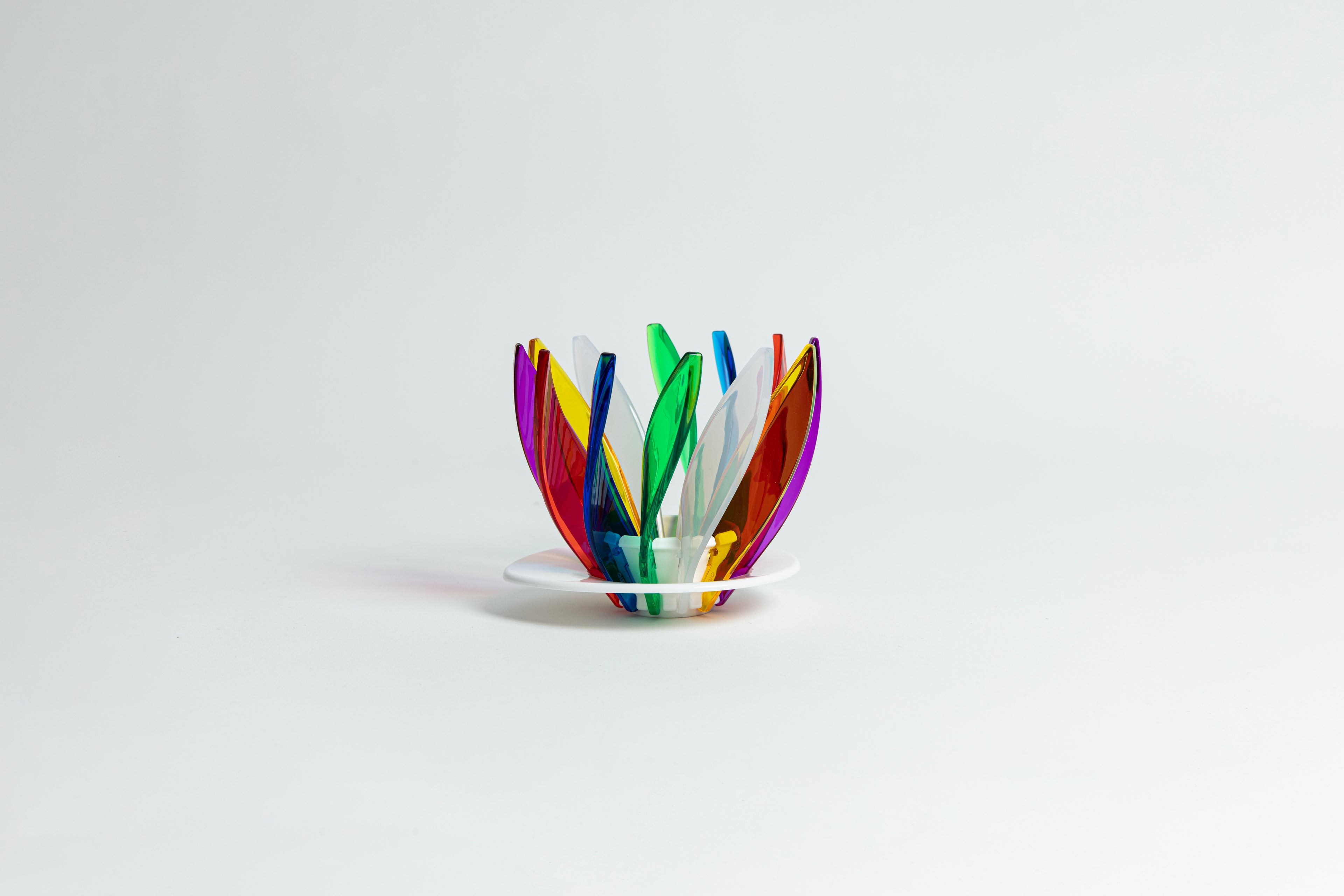 Transparent rainbow in the colors red, blue, green, white, orange, purple and yellow pedals in a spiral shape on a transparent black base on a white background.