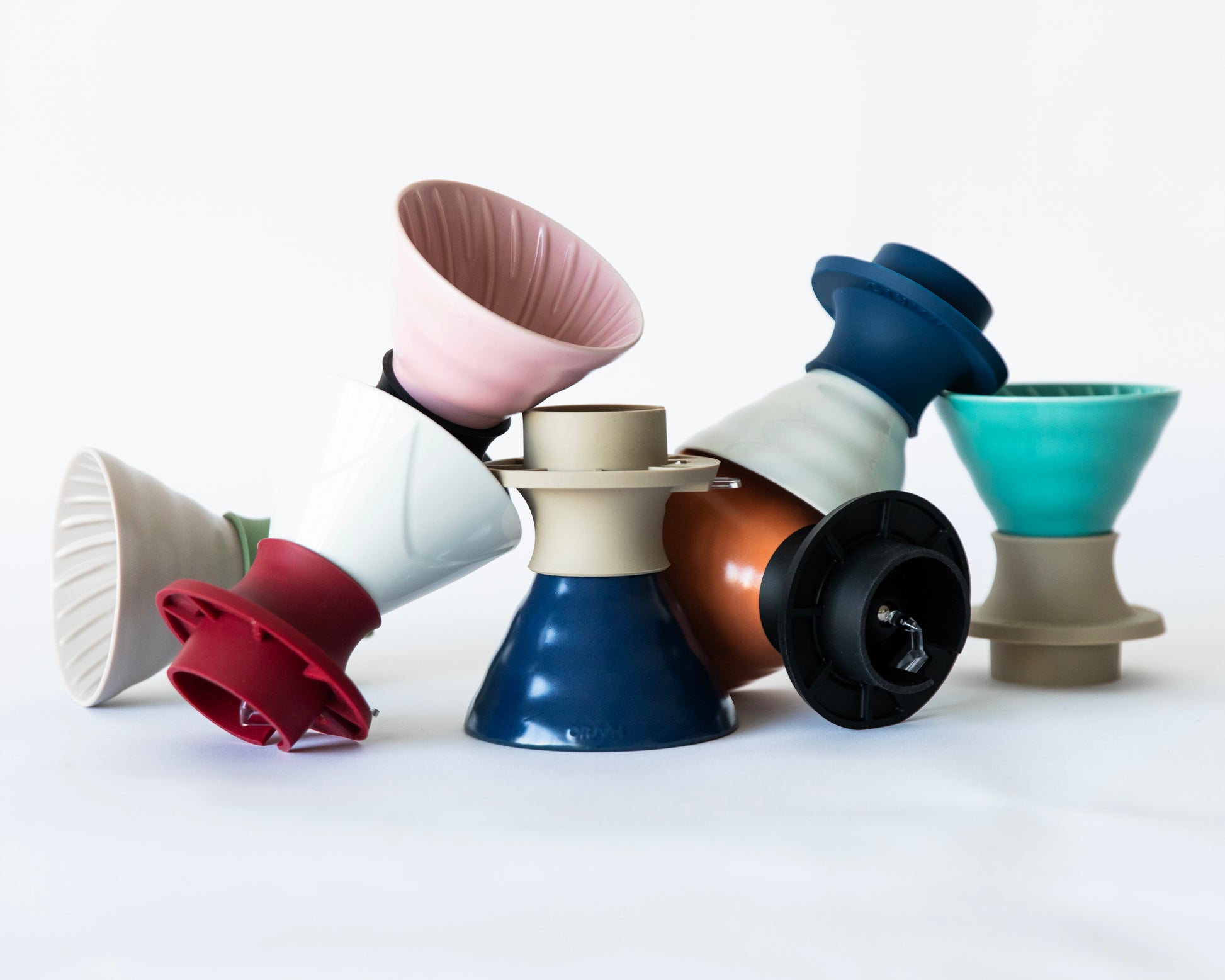 A colorful assortment of V60 ceramic cone coffee drippers with various silicone  bases, arranged in a pile on a white background. 