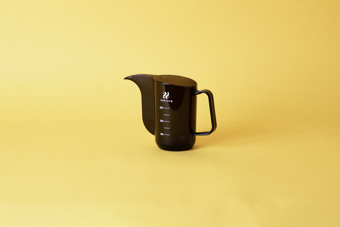 Transparent black plastic cup with handle and gooseneck style pour spout. set on yellow background