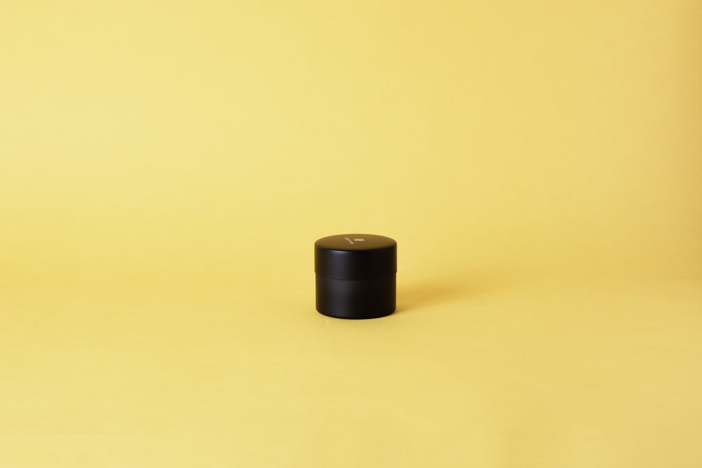 A black cylindrical container set on yellow background