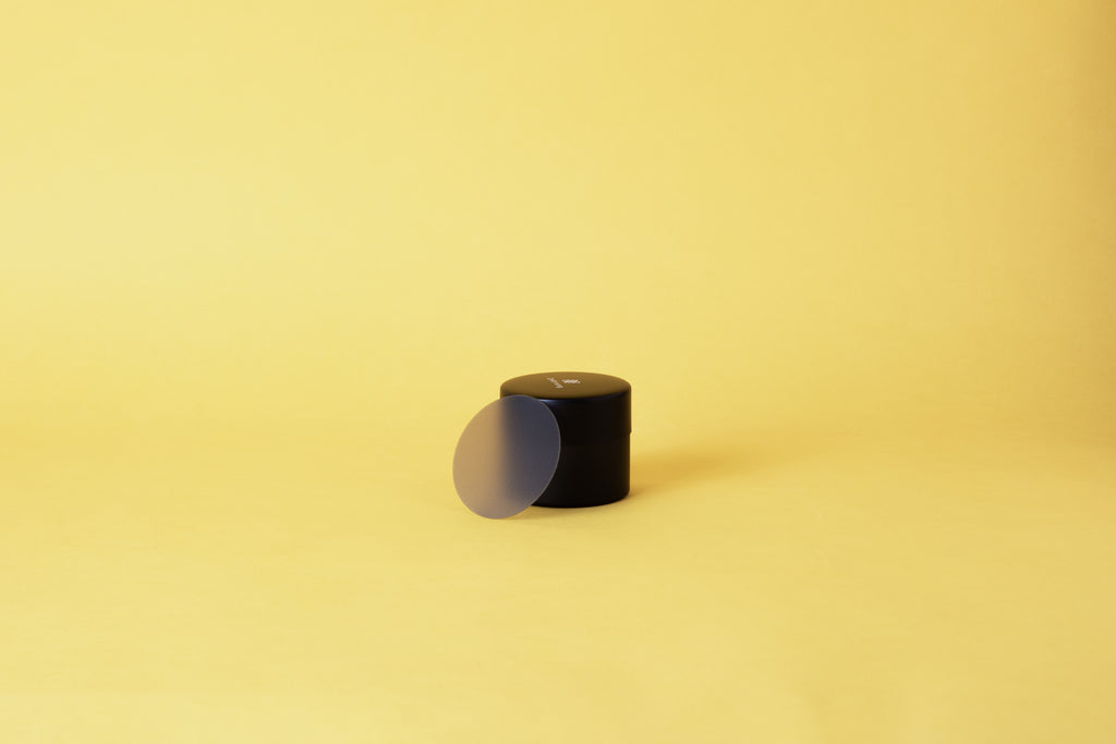 A black cylindrical container with a plastic disc. Set on yellow background