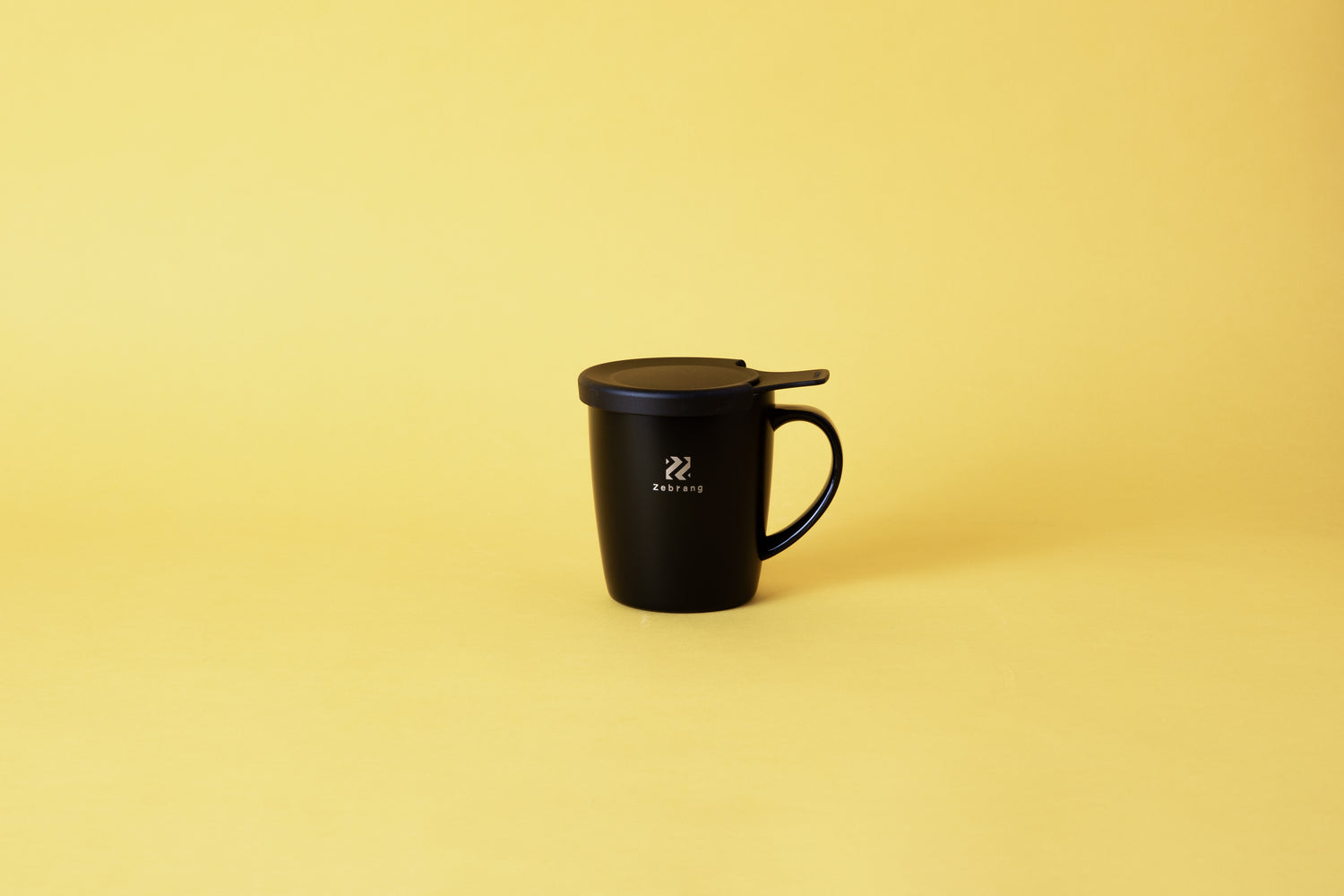 a black mug with a black lid and handle. set on yellow background