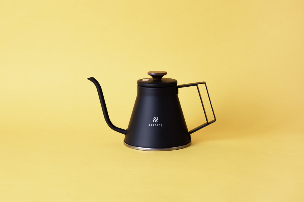black kettle kettle with gooseneck spout, square handle and flat, black plastic lid knob set on yellow background.