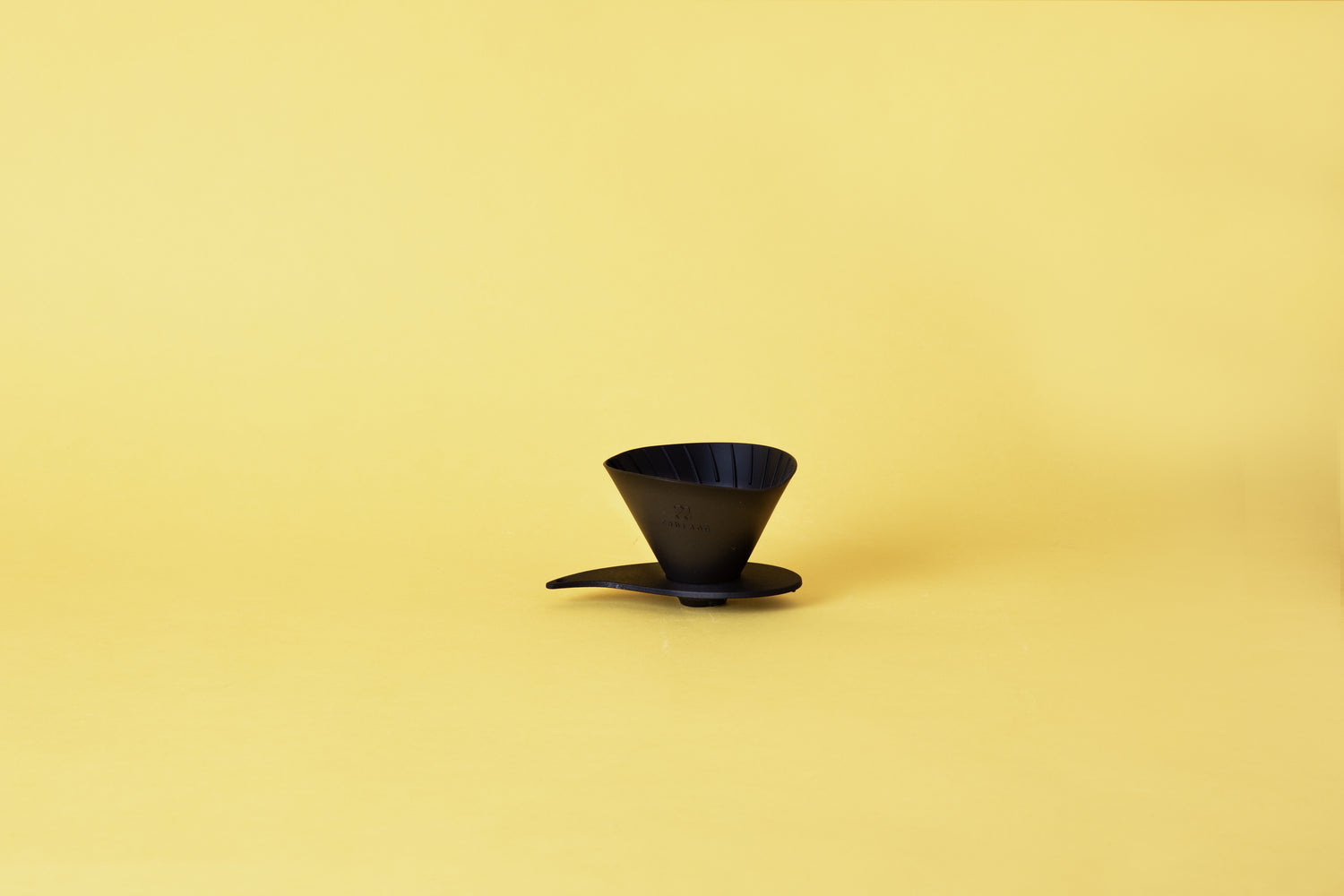 Silicone cone coffee dripper with ribbed spiral inside of the cone and placed on a plastic base. Set on yellow background.
