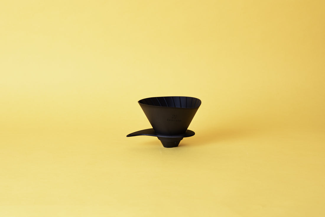 Silicone cone coffee dripper with ribbed spiral inside of the cone and placed on a plastic base. Set on yellow background.