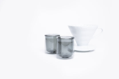 Two smoked glass tumblers and a white cone dripper with handle on a white background