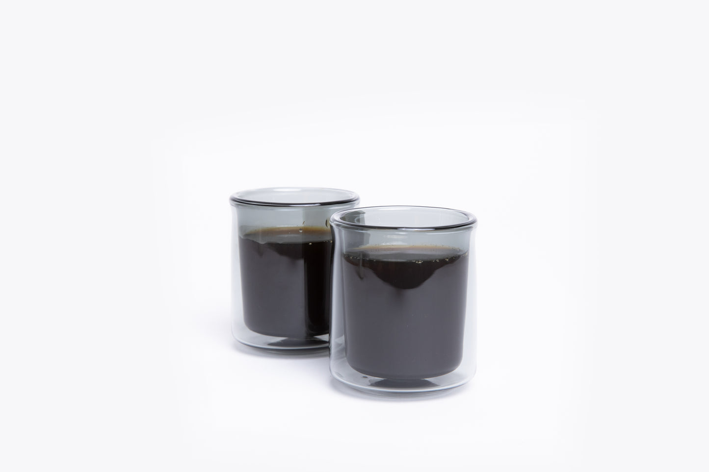 Two clear glass cups filled with black liquid on a white background