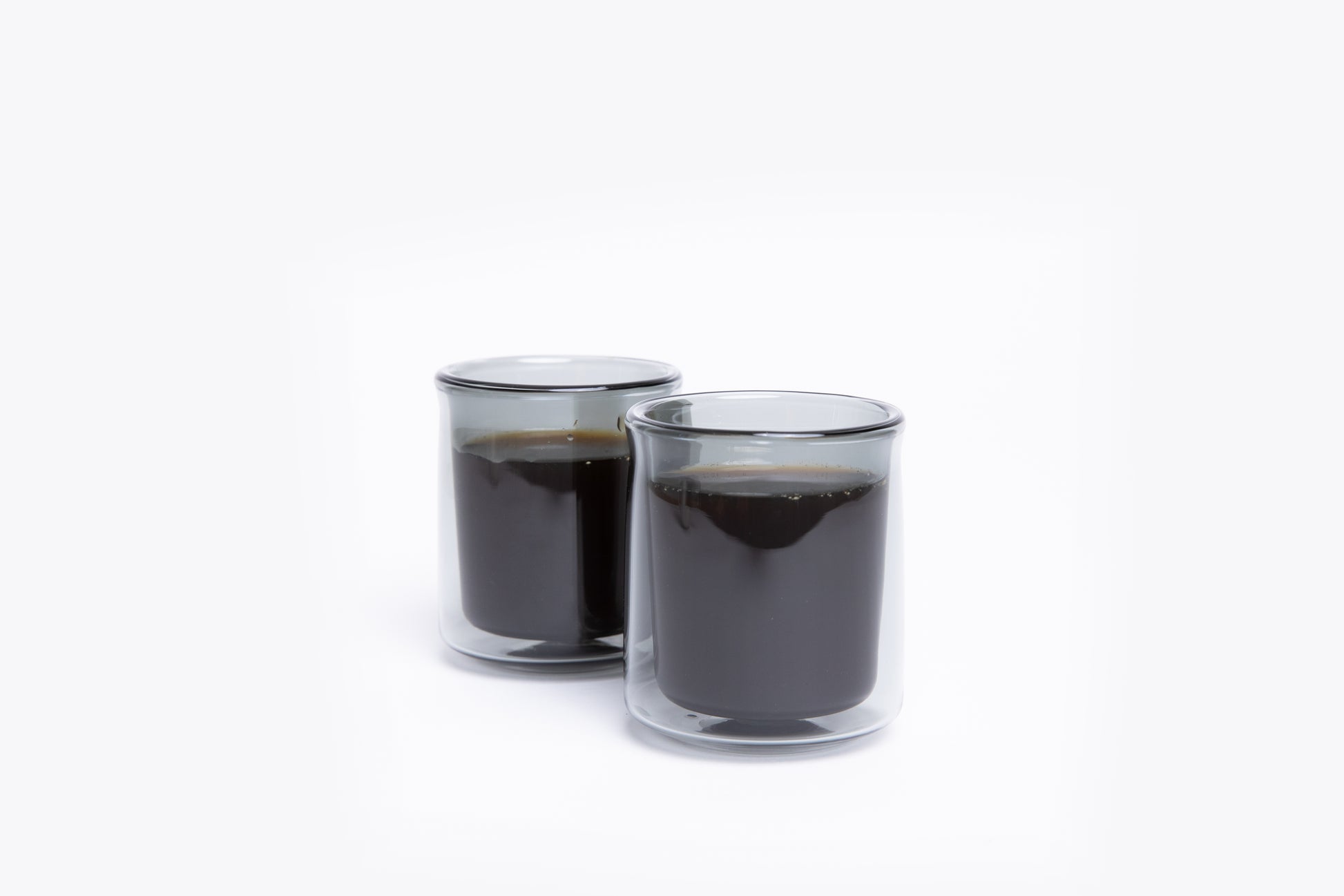 Two clear glass cups filled with black liquid on a white background