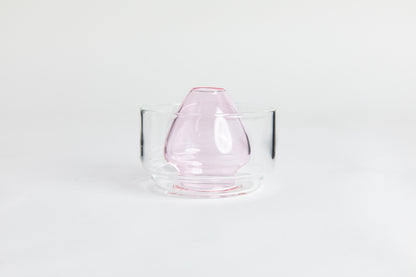 Dome-shaped pink clear glass matcha whisk holder with a smooth, tapered form, placed inside a clear glass base. Displayed on a white background with 'Hario' branding