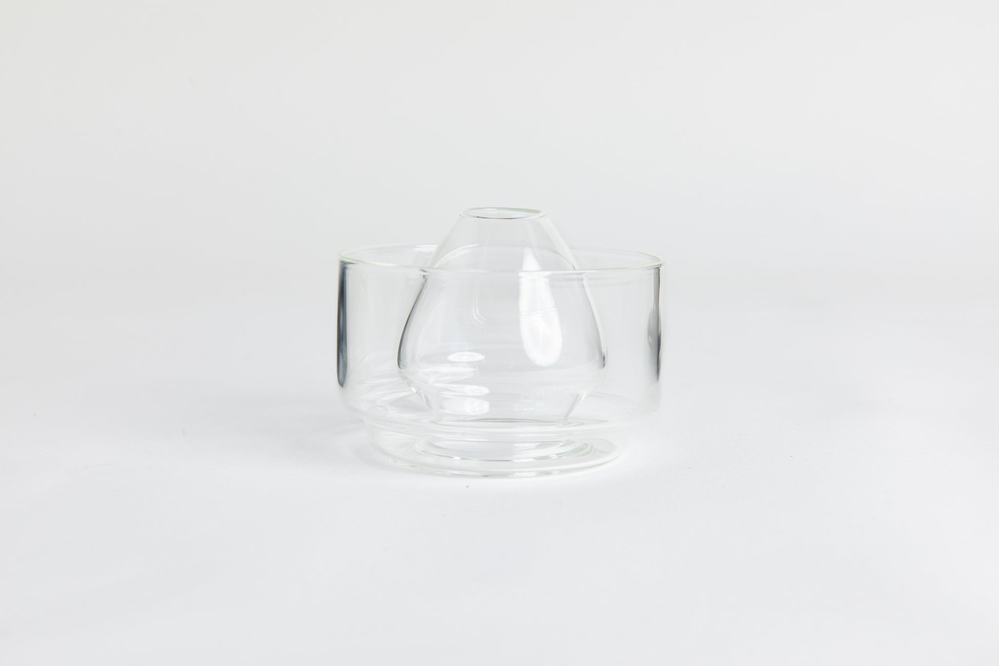 Dome-shaped clear glass matcha whisk holder with a smooth, tapered form, placed inside a clear glass base. Displayed on a white background with 'Hario' branding