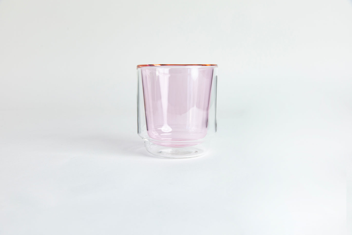 A clear double-walled glass with pink colored interior cup. set on a white background