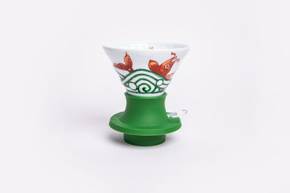 white cone dripper with gold fish design on a green silicone base on white background.