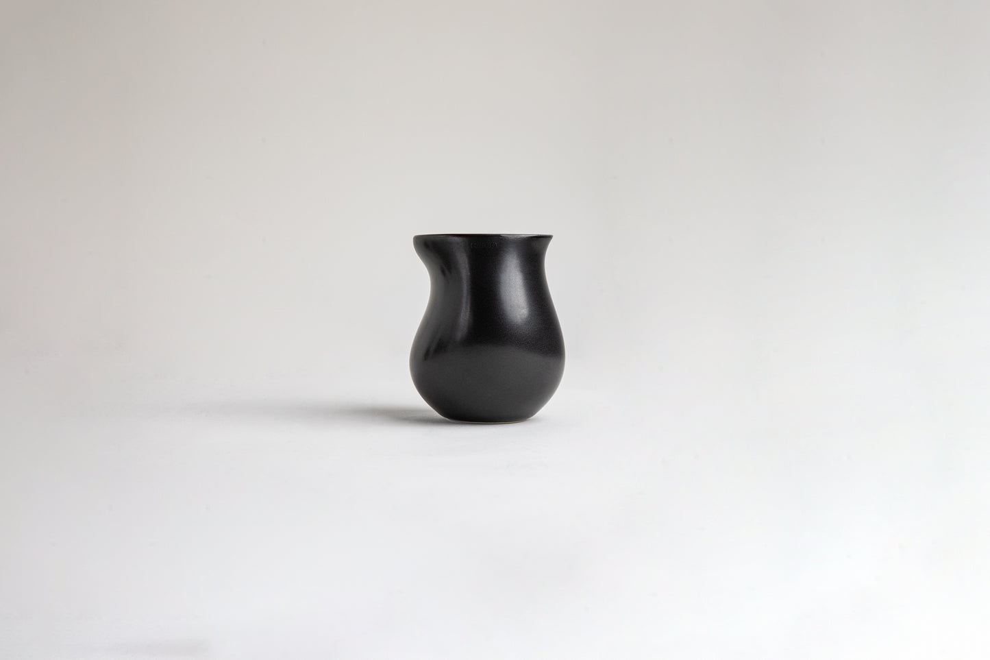Matte black ceramic vessel with a curvy, tulip-like silhouette. The surface has a smooth texture on a light gray background.