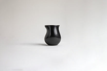 Matte black ceramic vessel with a curvy, tulip-like silhouette. The surface has a smooth texture on a light gray background.