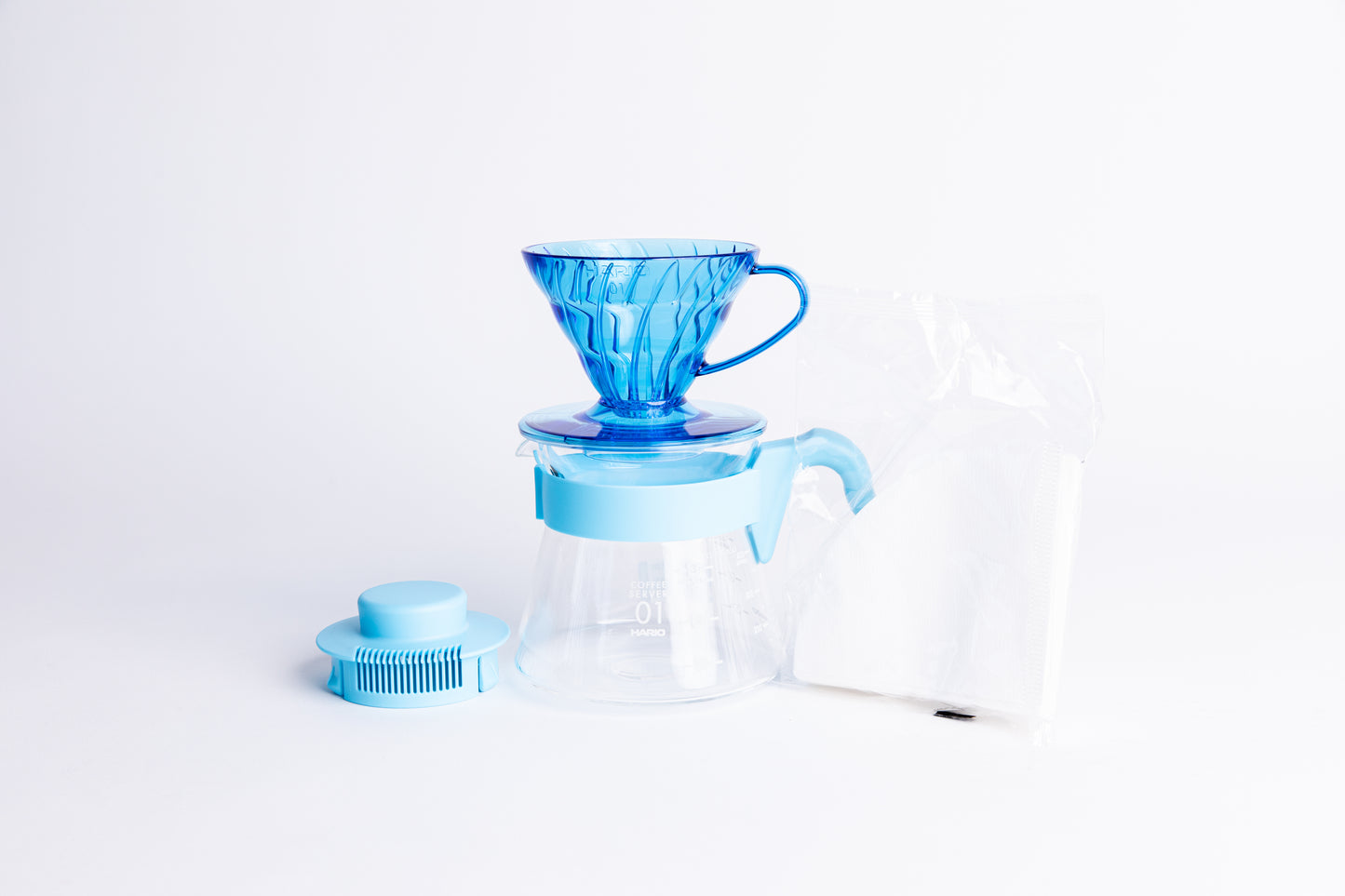 Transparent Blue plastic coffee cone dripper on glass server with light blue handle and lid with a pack of white filters on a white background
