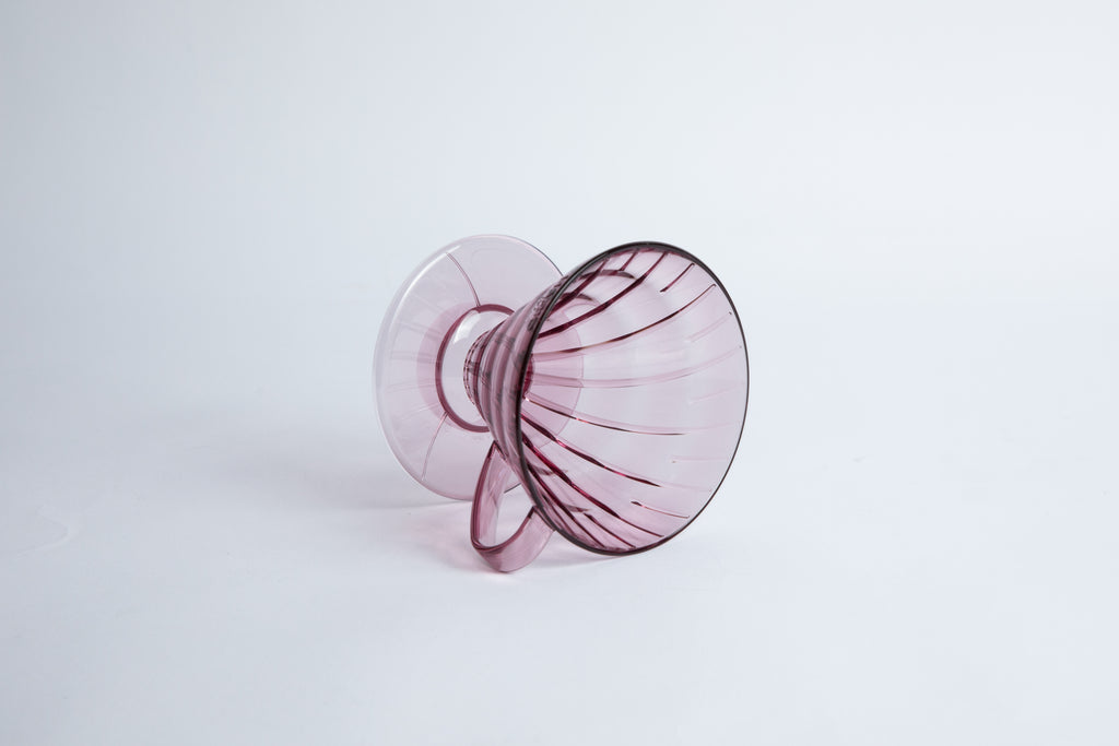 set on it's side the Size 02 Plastic V60 Dripper in the color transparent blushy mauve (Stardust) with a cylindrical base and curved handle. Set on a white background