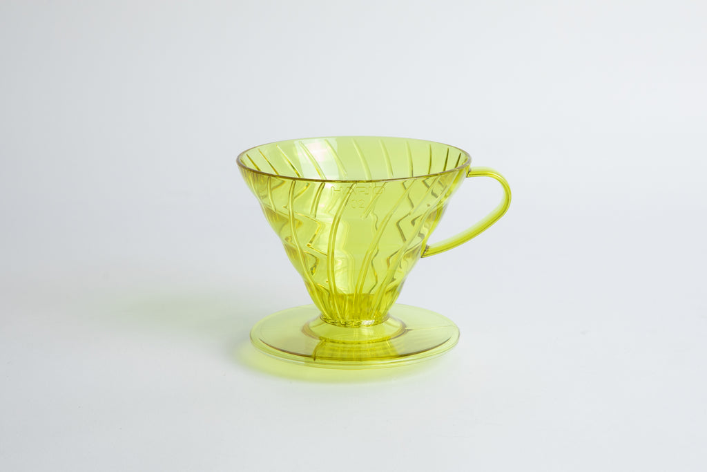 set on it's side the Size 02 Plastic V60 Dripper in the color transparent Chartreuse (Aurora) with a cylindrical base and curved handle. Set on a white background