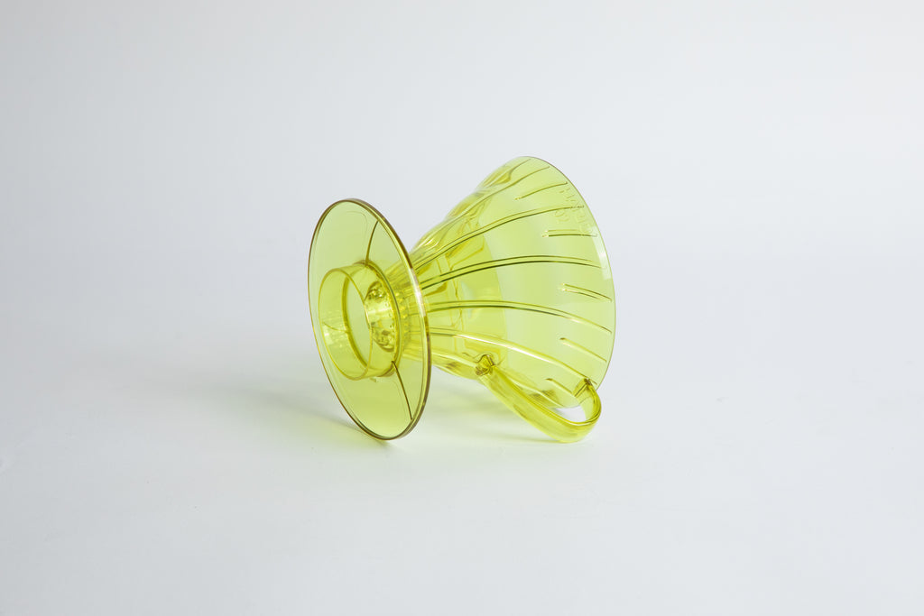 set on it's side the Size 02 Plastic V60 Dripper in the color transparent Chartreuse (Aurora) with a cylindrical base and curved handle. Set on a white background