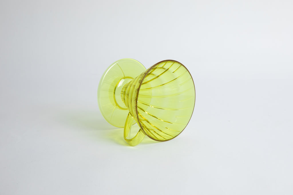 set on it's side the Size 02 Plastic V60 Dripper in the color transparent Chartreuse (Aurora) with a cylindrical base and curved handle. Set on a white background