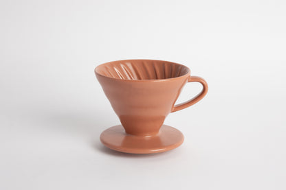Burnt Orange colored 60 degree cone shaped ceramic coffee dripper with handle and round base. Spiral ribbed on the inside cone. Set on white background