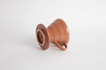 Burnt Orange colored 60 degree cone shaped ceramic coffee dripper with handle and round base. Set on white background