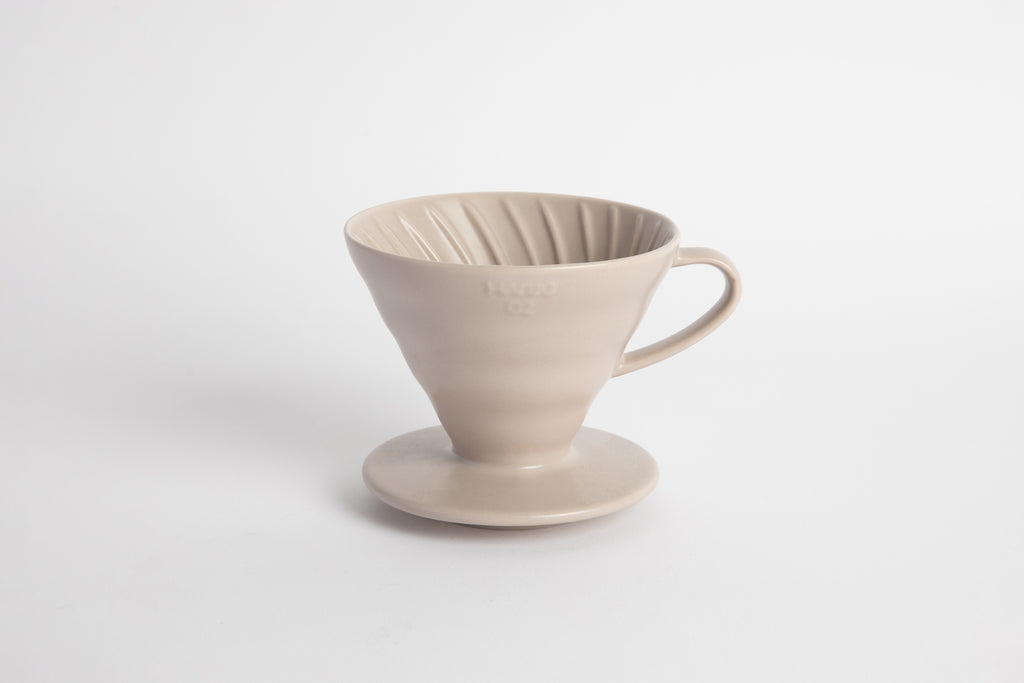 Off white colored 60 degree cone shaped ceramic coffee dripper with handle and round base. Spiral ribbed on the inside cone. Set on white background