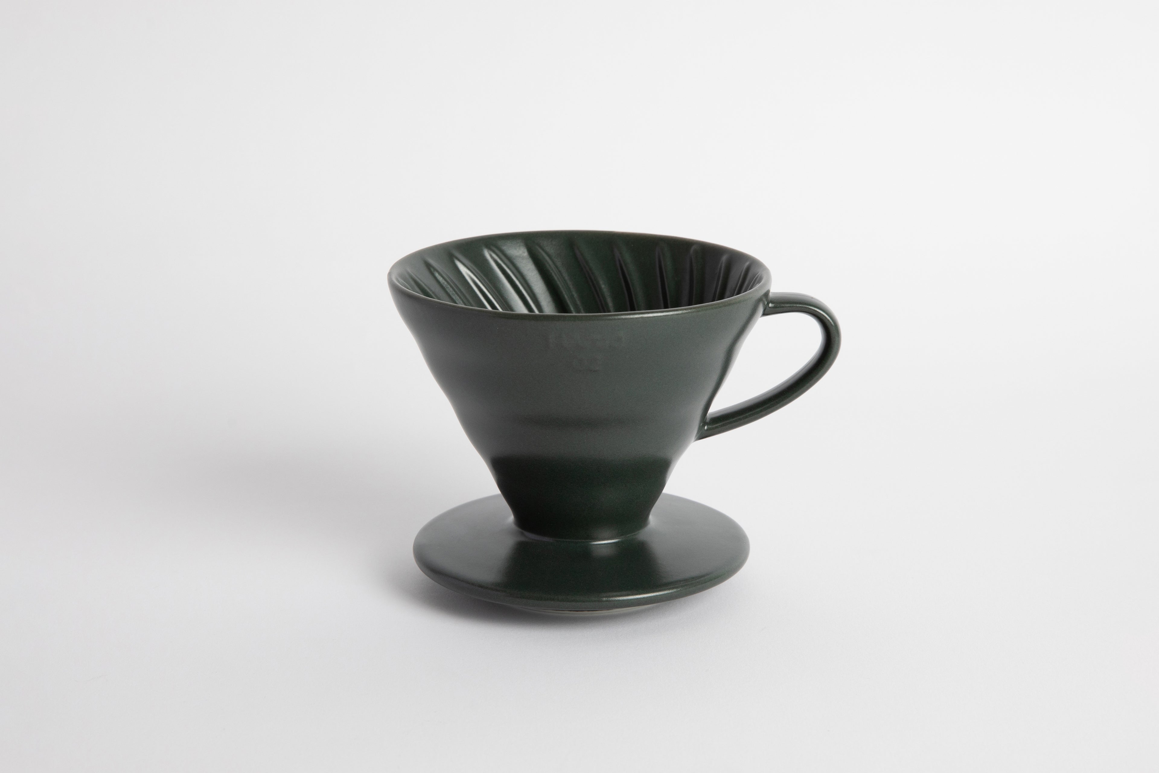 Dark Green colored 60 degree cone shaped ceramic coffee dripper with handle and round base. Spiral ribbed on the inside cone. Set on white background