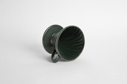 Dark green colored 60 degree cone shaped ceramic coffee dripper with handle and round base. Spiral ribbed on the inside cone. Set on white background